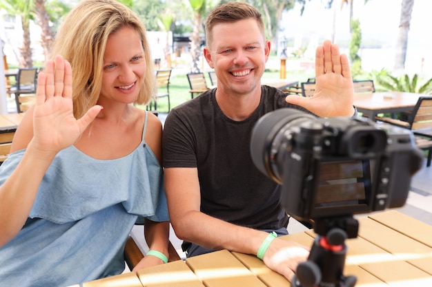 Mann und Frau sitzen am Tisch in der Bar und winken in die Kamera