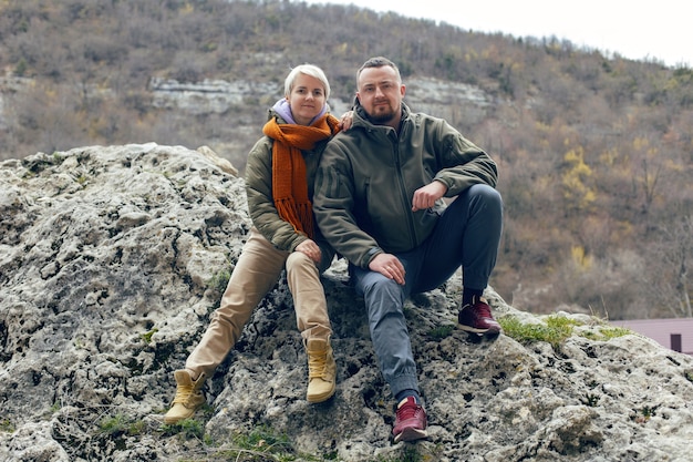 Mann und Frau sitzen im Herbst in warmer Kleidung auf einem Felsen