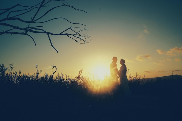 Mann und Frau stehen bei Sonnenuntergang auf dem Feld gegen den Himmel
