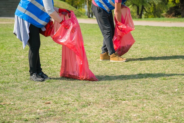 Mann und Frau tragen freiwillig das Aufsammeln von Müll und Plastikmüll im öffentlichen Park. Junge Leute, die Handschuhe tragen und im Freien Müll in rote Plastiktüten werfen