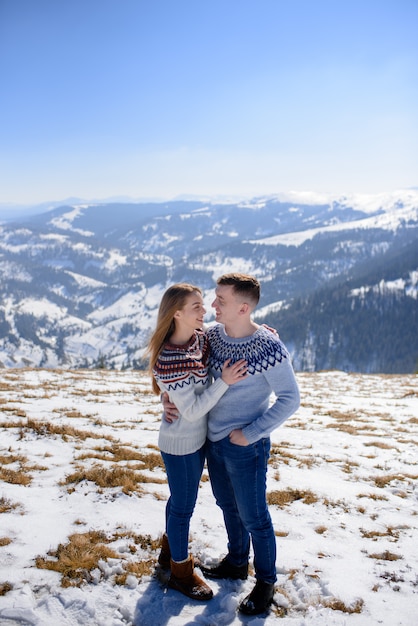 Mann und Frau tragen gestrickte Kleidung, die auf schneebedecktem Berg umarmt.