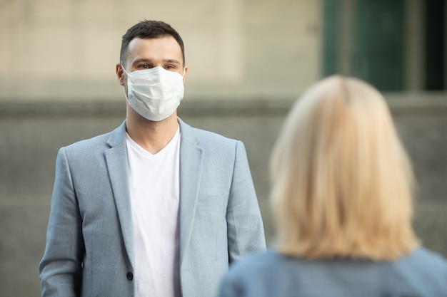 Mann und Frau tragen schützende Gesichtsmasken, die 2 m voneinander entfernt stehen und soziale Distanz halten, um die Ausbreitung des Coronavirus zu vermeiden
