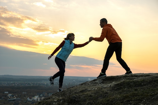 Mann und Frau Wanderer helfen sich gegenseitig, Stein bei Sonnenuntergang in Bergen zu klettern