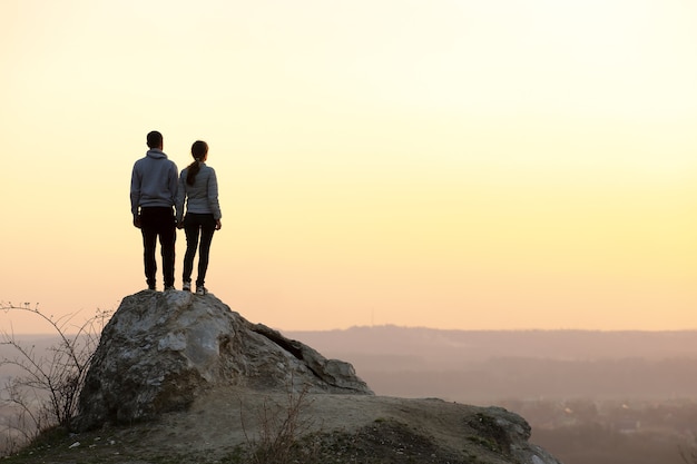 Mann- und Frauenwanderer, die bei Sonnenuntergang in den Bergen auf großem Stein stehen.