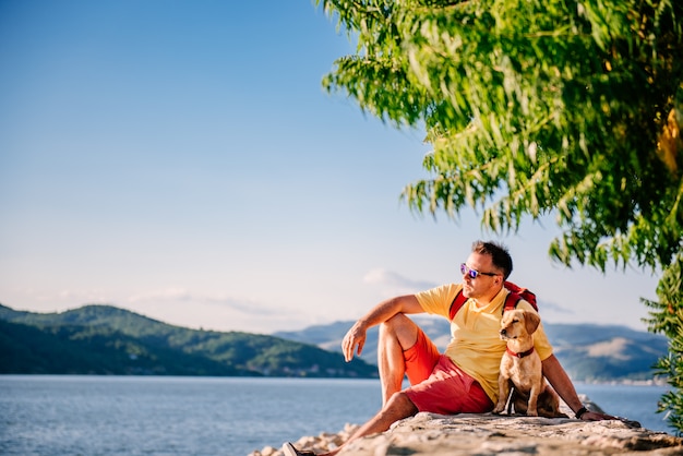 Mann und Hund sitzen auf einem steinernen Dock am Meer