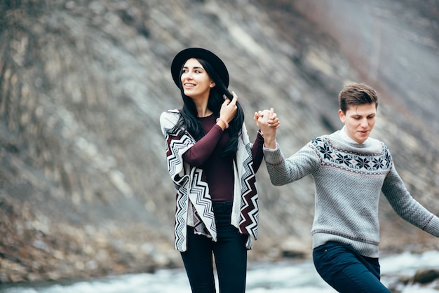 Mann und Mädchen in warmen Pullovern, die einen Bergfluss entlang gehen, Liebesgeschichte