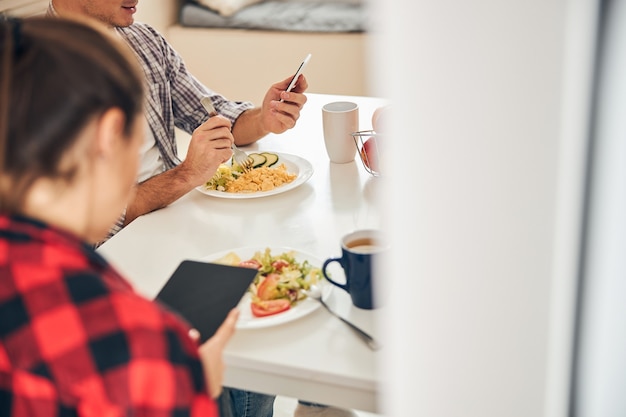 Mann und seine Frau, die beim Mittagessen Gadgets benutzen