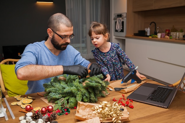 Mann und seine kleine Tochter lernen, einen Weihnachtskranz online zu dekorieren