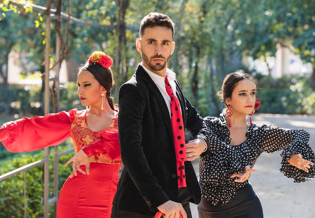 Mann und zwei Frauen in traditioneller Flamenco-Kleidung tanzen Flamenco in einem Park mit Pflanzen