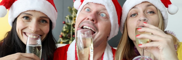 Mann und zwei Frauen in Weihnachtsmann-Hüten trinken Champagner für das neue Jahr