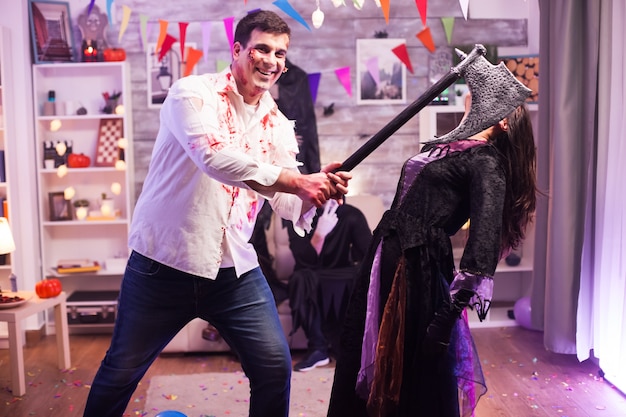 Mann verkleidet wie ein Zombie mit einer Axt, der versucht, eine böse Hexe auf einer Halloween-Party zu töten.
