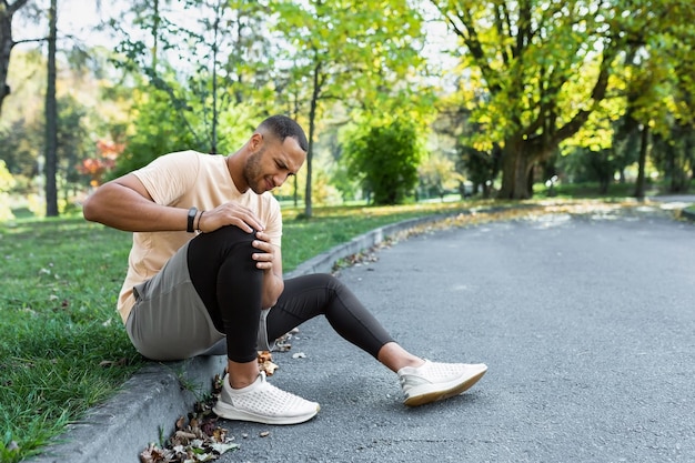 Mann verletztes Bein beim Joggen Afroamerikanischer Mann sitzt auf dem Boden und massiert Muskelkater mit