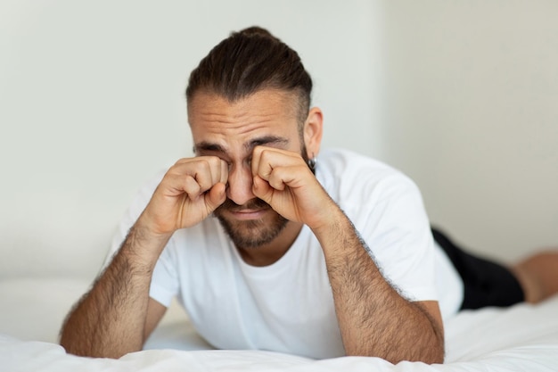 Mann wacht nach einer schlaflosen Nacht im Bett auf und reibt sich die Augen