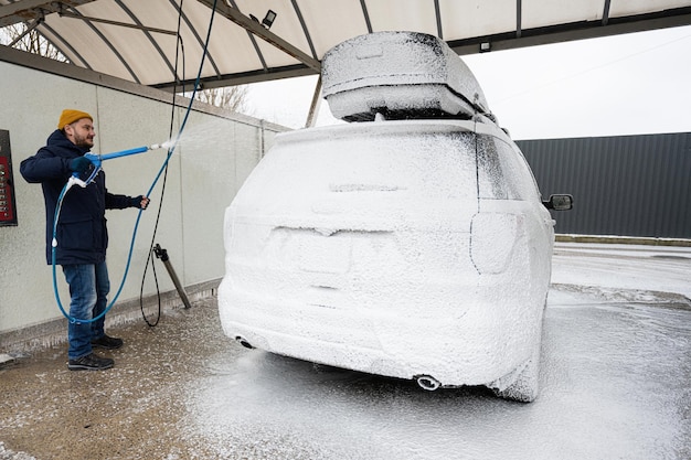 Mann wäscht amerikanisches SUV-Auto mit Dachgepäckträger bei einer Selbstbedienungswäsche bei kaltem Wetter