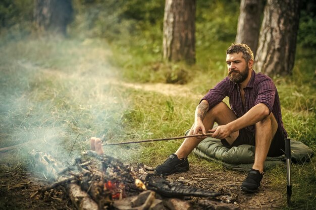 Mann Wanderer Bratwürste am Stock auf Lagerfeuer im Wald