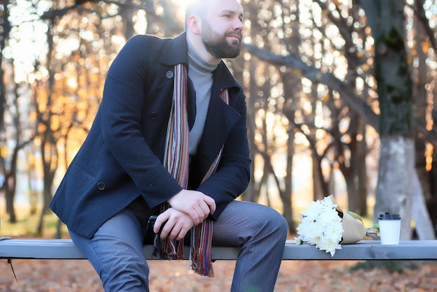 Mann wartet auf einer Bank das Datum im Herbstpark mit Blume