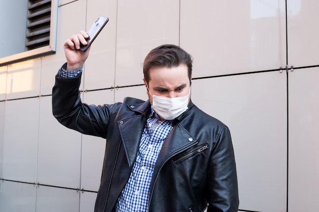 Mann will sein Smartphone brechen, Geschäftsmann, der Schutzmaske mit Smartphone, Gesundheitskonzept trägt. Coronavirus Quarantäne.