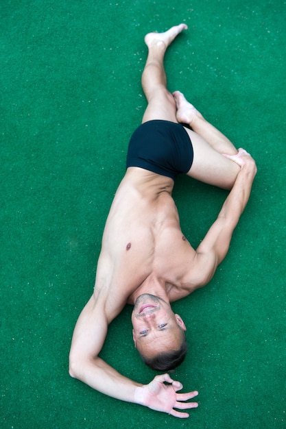 Mann Yoga-Praxis-Pose grüne Oberfläche Draufsicht. Athlet macht Yoga Asana auf grünem Hintergrund. Üben des Asana-Konzepts. Kerl muskulöser flexibler Körper. Flexibilitätstraining dehnt Muskeln und Gelenke.