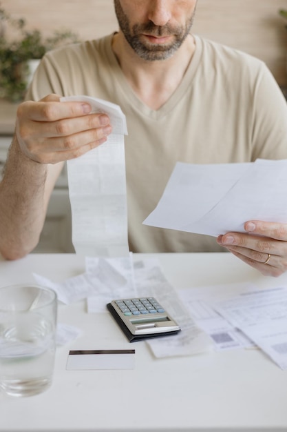 Mann zahlt Rechnungen und Nebenkosten zählt die Höhe der Ausgaben und Einnahmen auf dem Rechner Finanzielle Bildung und Hypotheken- oder Mietzahlung