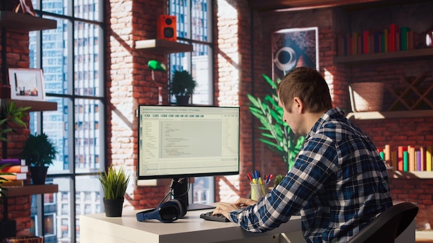 Mann zu Hause, der sich die Benutzeroberfläche auf dem PC-Bildschirm ansieht, programmiert und programmiert
