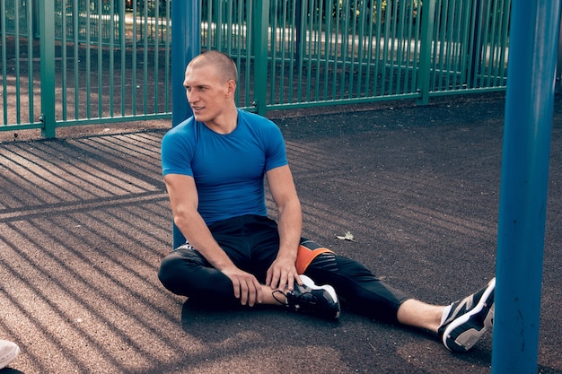 Mannathlet, der nach dem Training im Freien auf dem Boden sitzt