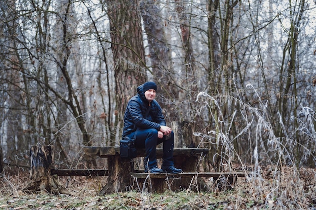 Mannfotograf, der auf der Bank im Wald sitzt und sich darauf vorbereitet, ein Bild der Landschaft in den Bergen zu machen. Mann, der den Ort mit Vergnügen betrachtet