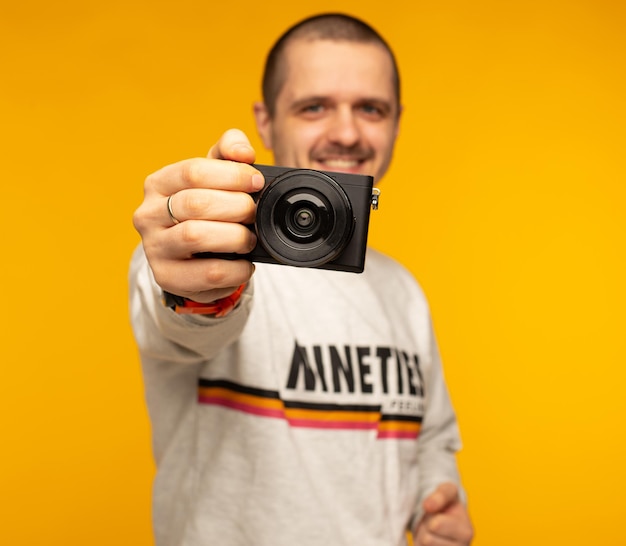 Mannfotograf, der eine spiegellose Kamera in der Hand hält und auf orangefarbenem Hintergrund lächelt