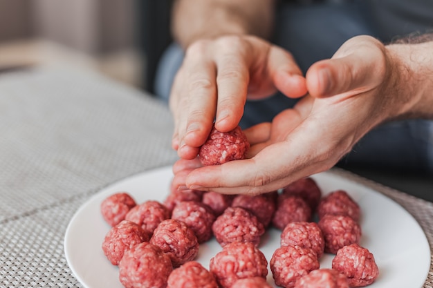 Mannhände, die Fleischbällchen mit rohem Hackfleisch vorbereiten