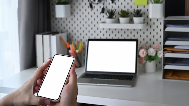 Mannhände halten Smartphone mit weißem Bildschirm und sitzen im Home Office.