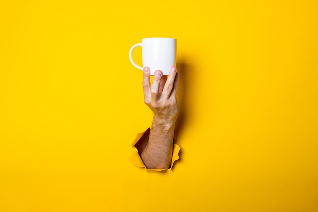 Mannhand, die eine weiße Tasse auf einem hellen gelben Hintergrund hält