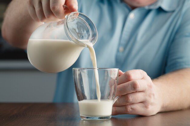 Mannhand, die Milch vom Glas in Glas fließt