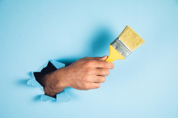 Mannhand, die pinsel auf blauem hintergrund hält