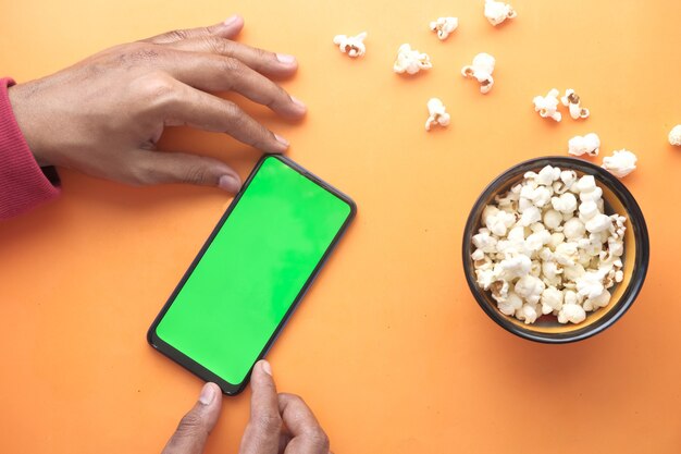 Mannhand, die Smartphone und Popcorn isst.