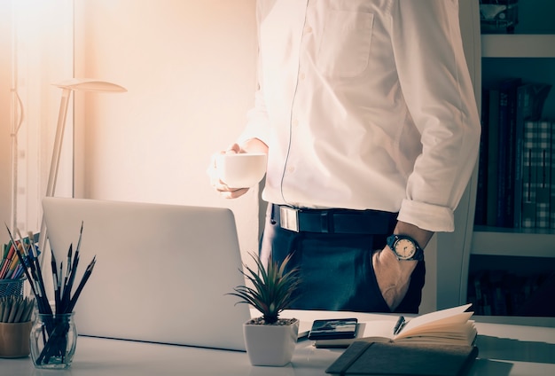 Mannhand, die Tasse Kaffee stehend im Büro hält