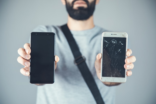 Mannhand neues und kaputtes Telefon auf grau