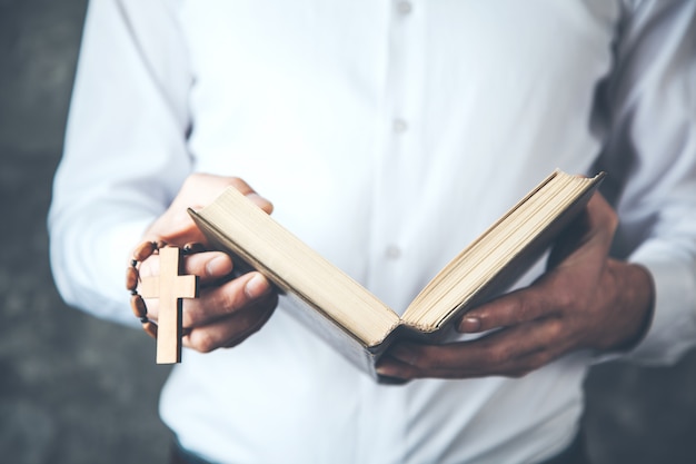 Mannhandkreuz mit Buch auf dunklem Hintergrund