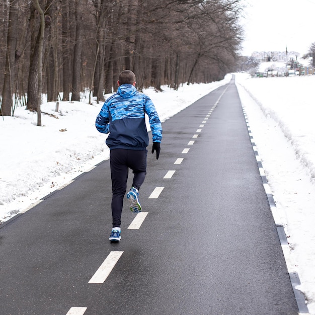 Mannläufer, der im Winter auf der Strecke läuft. Outdoor-Training und Workout