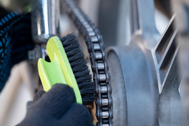 Mannliche Hände in Handschuhen reinigen die Kette eines Motorrads aus der Nähe