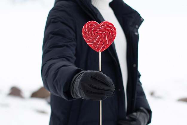 Foto mannliche hand hält einen roten lolly in form eines herzens auf schnee-hintergrund