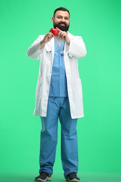 Mannlicher Arzt in voller Länge auf grünem Hintergrund zeigt ein Herz