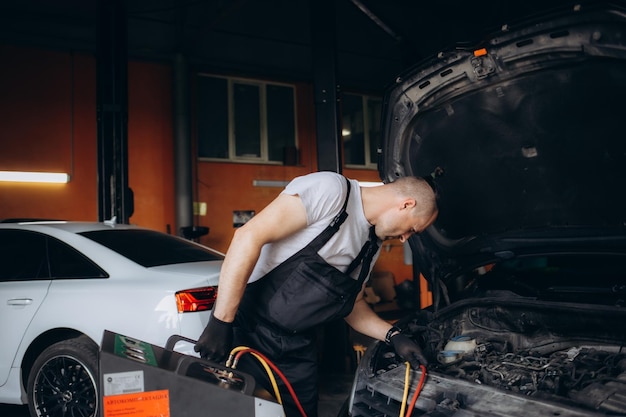 Mannlicher Automechaniker füllt die Klimaanlage des Autos auf und überprüft das Kompressor-Ölsystem, das durch die Klimanlage des Autos verursacht wird, ist nicht kalt