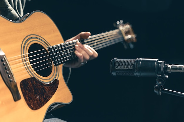 Mannlicher Musiker spielt Akustikgitarre hinter einem Mikrofon im Aufnahmestudio