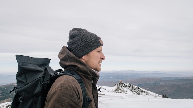 Mannlicher Wanderer steht auf einem schneebedeckten Berg gegen den Himmel