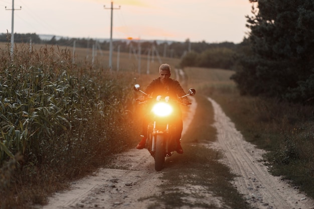 Mannreisender, der ein Motorrad mit Licht im Feld reitet