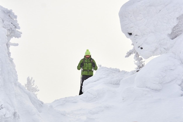 Mannreisender in den Winterbergen unter den schneebedeckten Klippen während eines Schneesturms