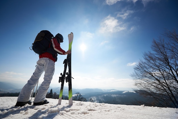 Mannskifahrer mit den Skiern und Rucksack, die im weißen Schneewintergebirgslandschaftshintergrund stehen