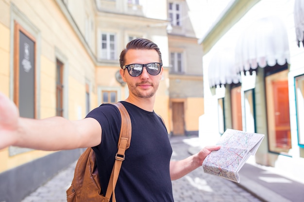 Manntourist mit einem stadtplan und einem rucksack in europa-straße. kaukasischer junge, der mit karte der europäischen stadt schaut.