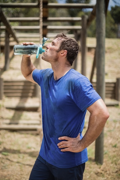 Manntrinkwasser aus Flasche während des Hindernislaufs im Bootcamp