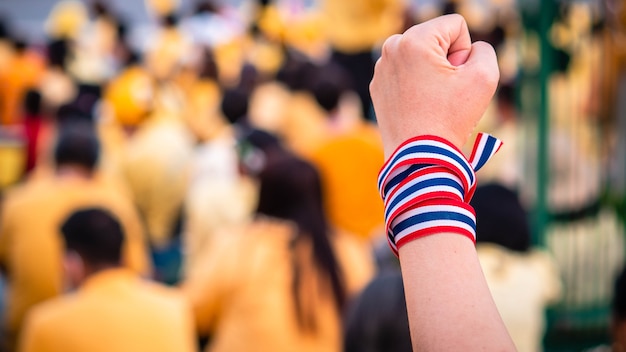 La mano adulta envuelve la bandera tailandesa de fondo borroso tailandés en apoyo de la monarquía de Tailandia.