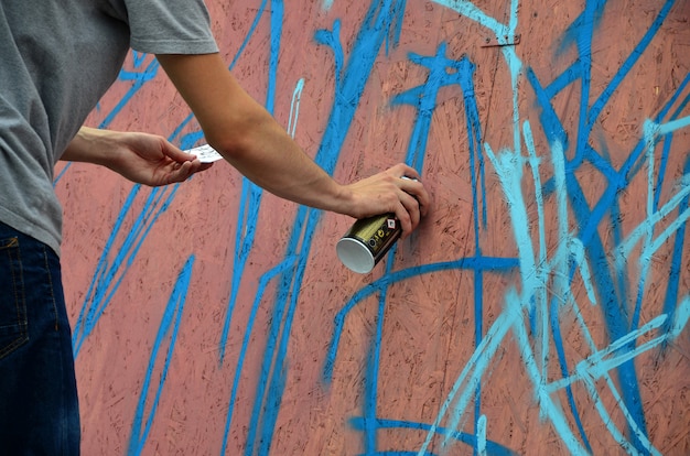 Una mano con un aerosol que dibuja un nuevo graffiti en la pared.